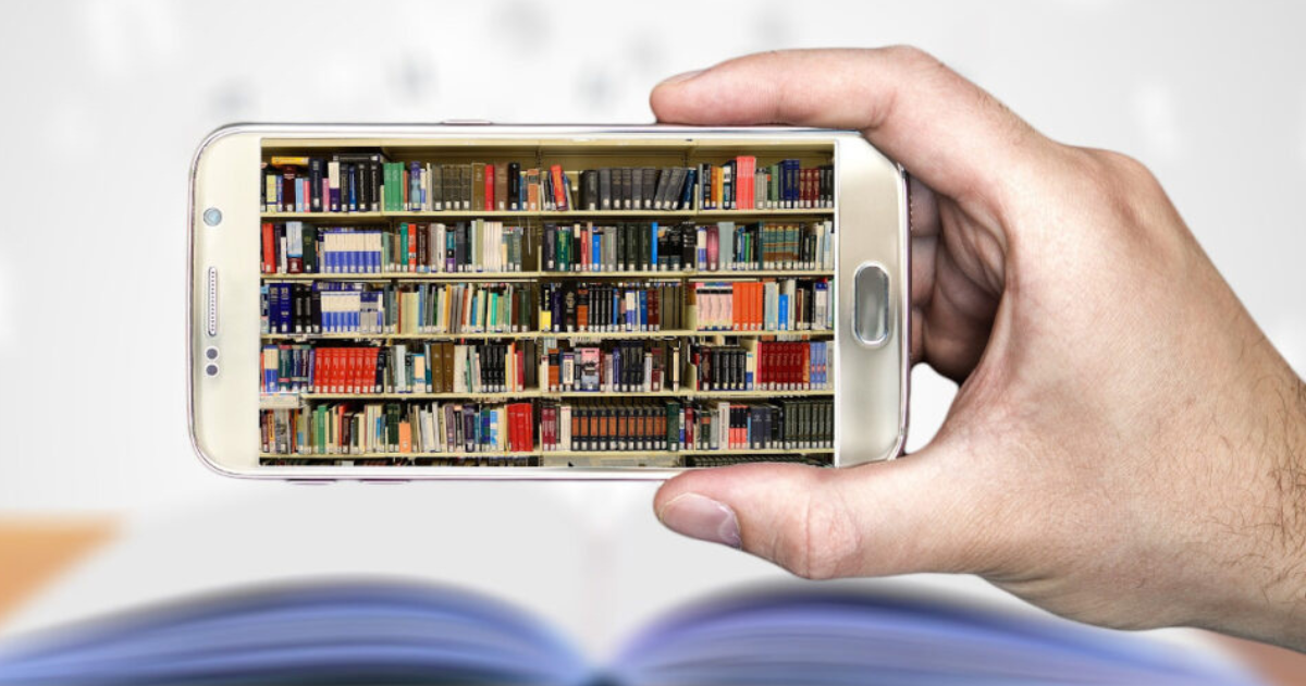 Dłoń trzyma smartfon, na którym wyświetlają się biblioteczne półki z książkami